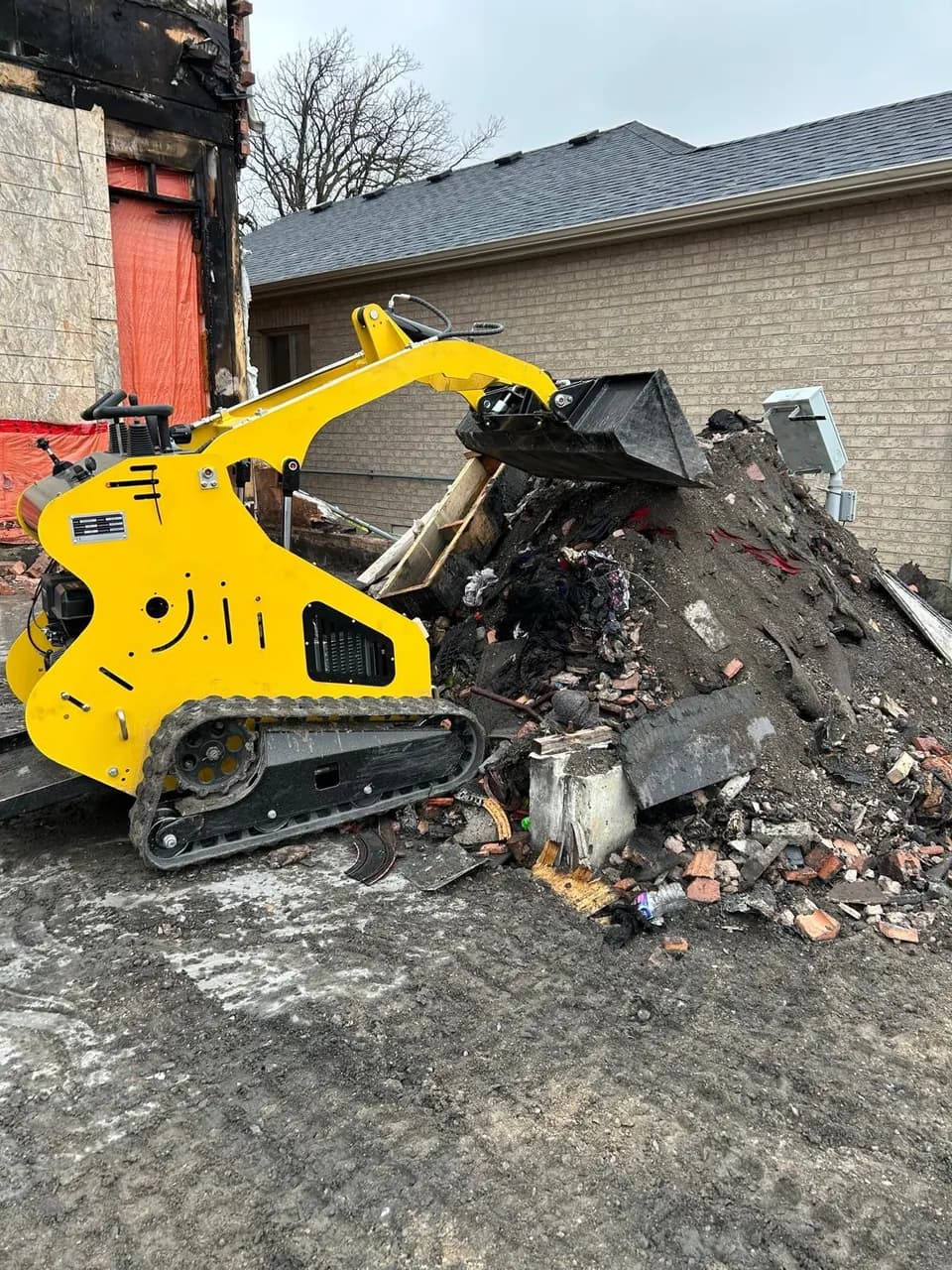 Our mini stand-on track loader scooping debris onto a pile during a residential cleanup job.